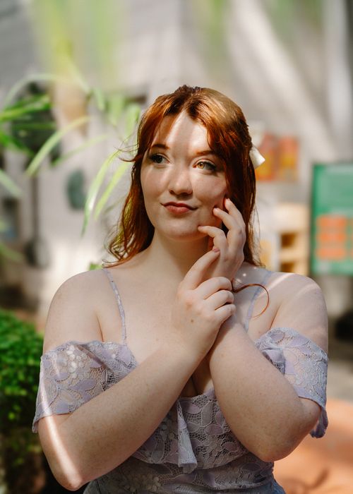 Free A serene portrait of a woman in a stylish dress with sunlit highlights, set in a lush garden environment. Stock Photo