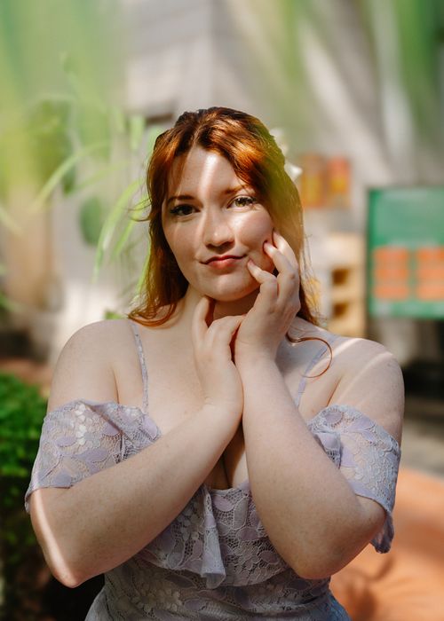 Free Portrait of a redhead woman in a lacy dress posing in sunlight at a garden. Stock Photo