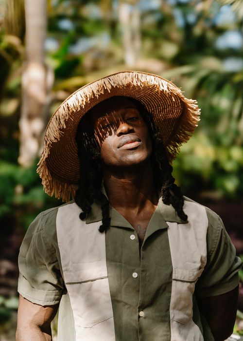 Free African man in a straw hat, shot outdoors in a vibrant tropical setting, showcasing natural elegance. Stock Photo