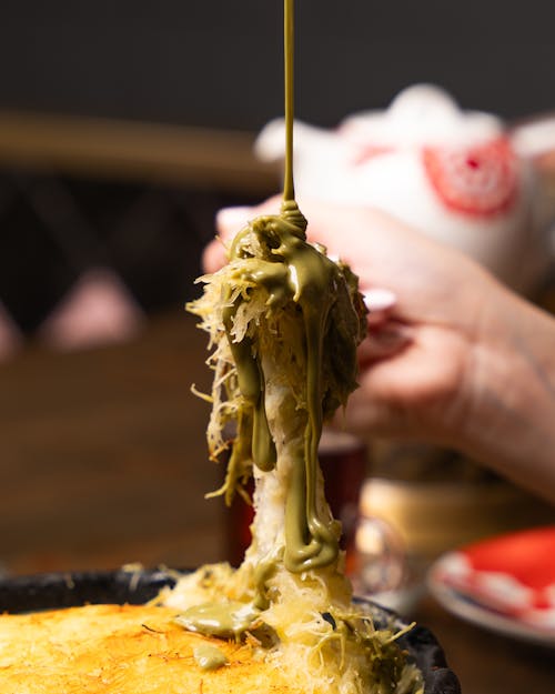 A person is holding a piece of food with a green sauce