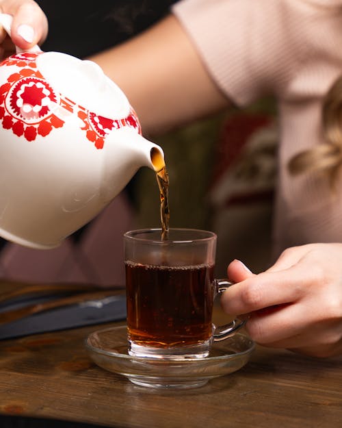 A woman pouring tea into a cup with a red lid