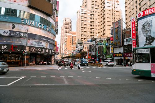 Free Busy urban intersection in Taipei, with scooters and buses under towering buildings. Stock Photo