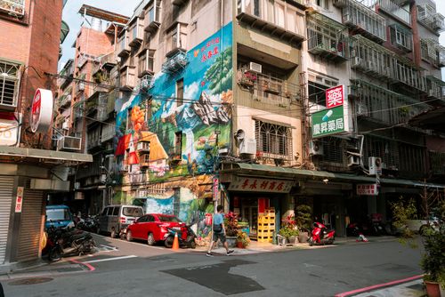 Free Colorful mural depicting nature on a city street building with parked scooters and cars. Stock Photo