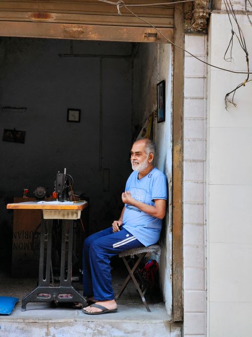 Free Portrait of a smiling elderly tailor in a blue shirt, enjoying a break outside his workshop in Ahmedabad. Stock Photo