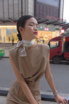 Elegant model in beige attire posing stylishly on city street with closed eyes.