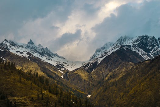 Scenic view of snow-capped mountain peaks beneath a dramatic cloudy sky, capturing nature's grandeur.