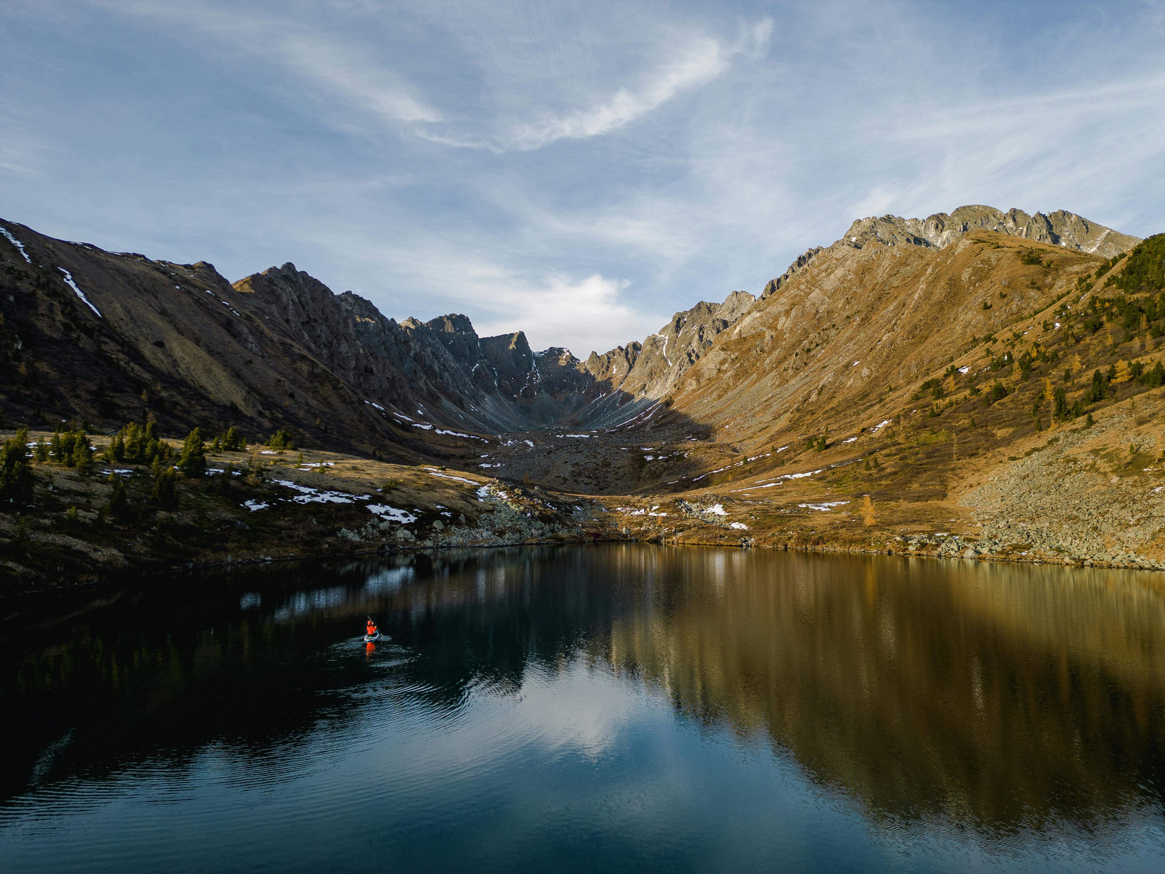 A tranquil mountain lake reflecting a kayaker under a serene sky.