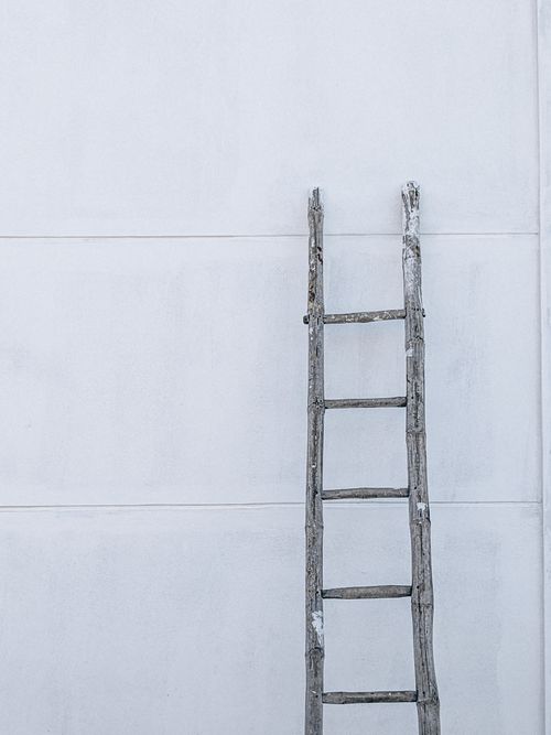 Free A rustic wooden ladder leaning against a plain white wall in a minimalist style. Stock Photo