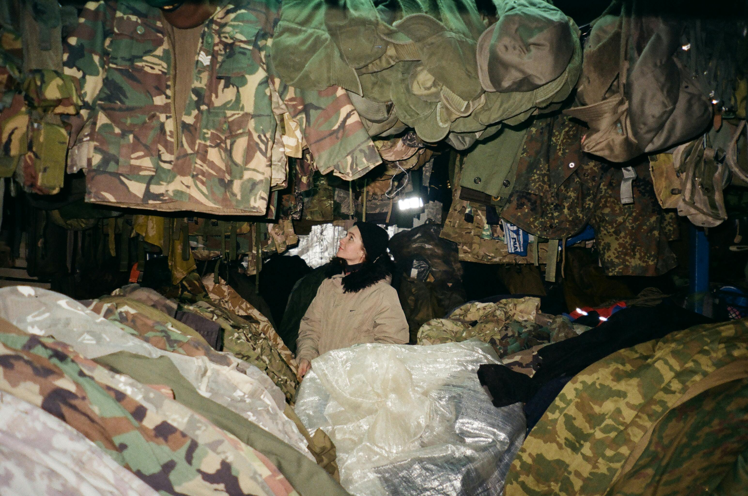 A woman looks up at various military camouflage jackets and gear indoors.