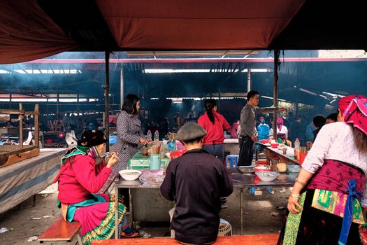 A lively traditional food market with people enjoying street food under a tent.