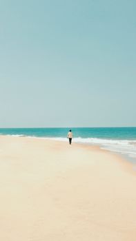 A lone person walks along a vast, tranquil beach under a clear summer sky.