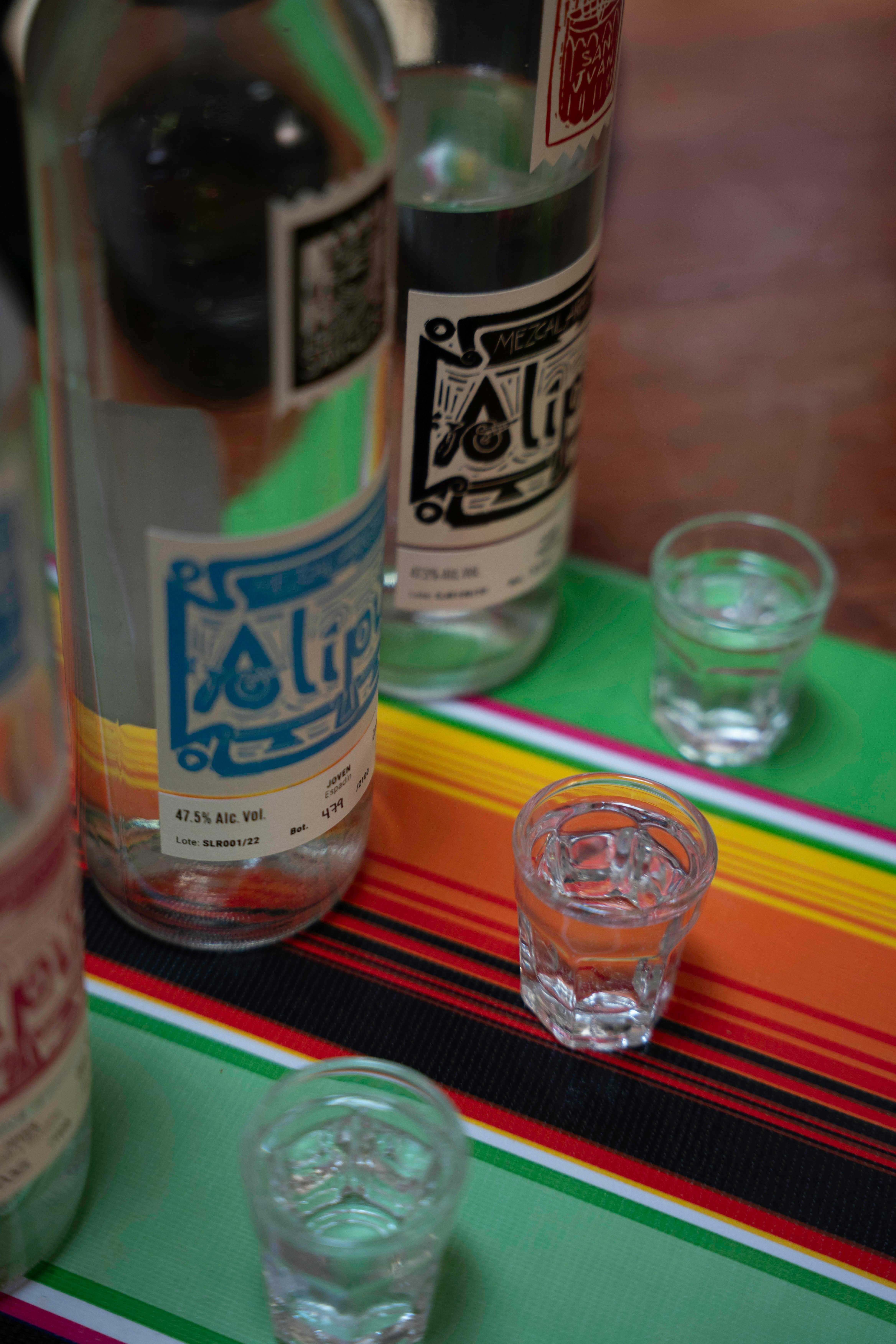 Vibrant shot of mezcal bottles and glass cups on a colorful striped tablecloth, perfect for festive themes.