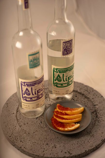 A glass bottle filled with amber-orange homemade triple sec next to curls of fresh orange zest and a small pour glass.