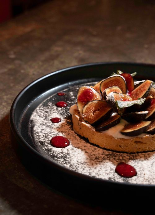 Free A freshly prepared fig tart with a dusting of sugar and berry coulis on a dark plate. Stock Photo
