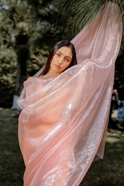 Elegant portrait of a woman draped in shimmering pink fabric, captured outdoors in a natural setting.