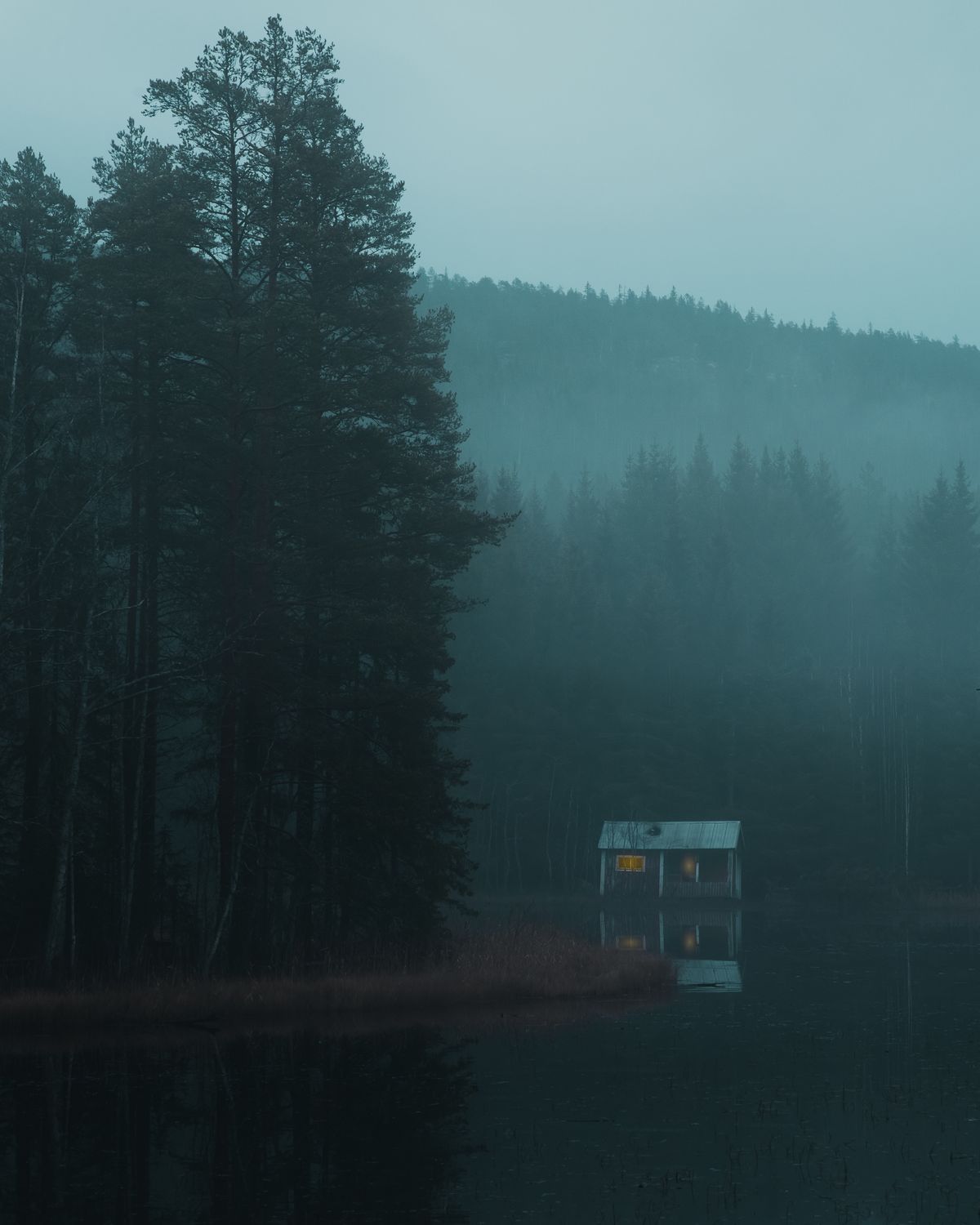 A wooden cabin reflected in a still Swedish lake at dawn — the kind of shoreline Allemansrätten makes freely available to every visitor