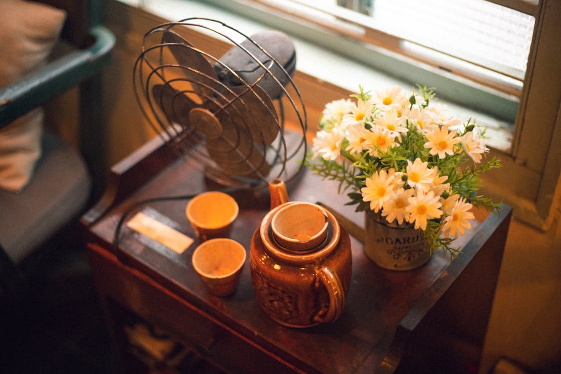 Free Blooming White and Yellow Daisy Flowers Near Brown Teapot Beside Desk Fan on Table Stock Photo