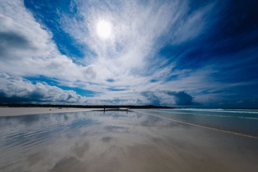 Breathtaking beach scene with a mirrored shoreline under a vast blue sky and bright sun.