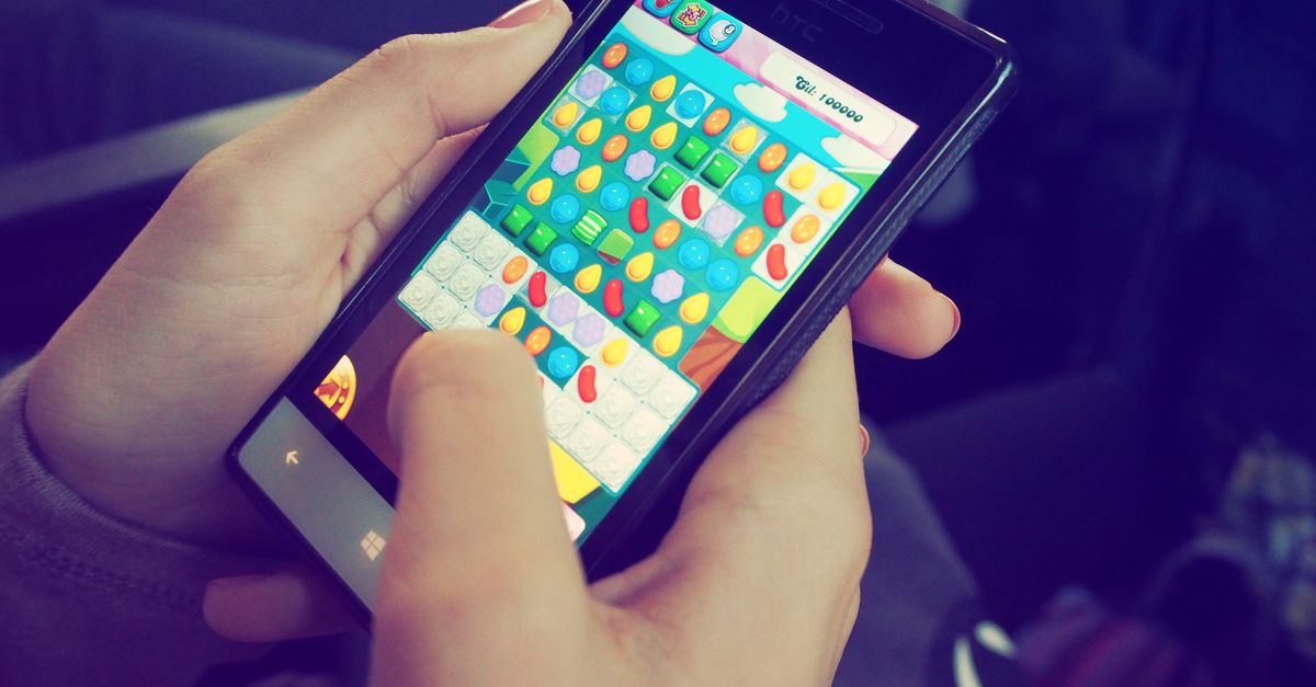 Mãos segurando um smartphone com um jogo de quebra-cabeça colorido na tela, exibindo tecnologia moderna.
