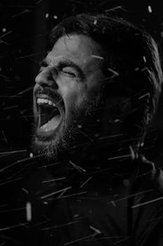 Dramatic black and white close-up portrait of a man shouting with closed eyes.