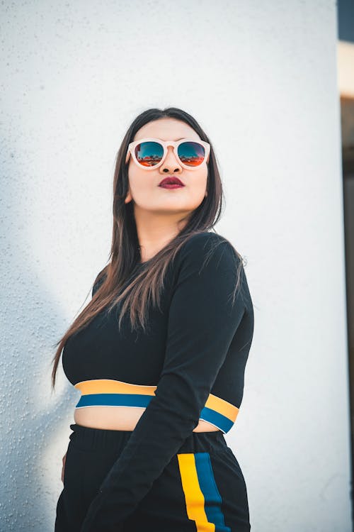 Photo of Woman in Sunglasses and Black Outfit Standing Beside White Wall