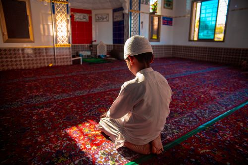 Free A young boy in a white outfit kneeling and praying inside a vibrant mosque. Stock Photo