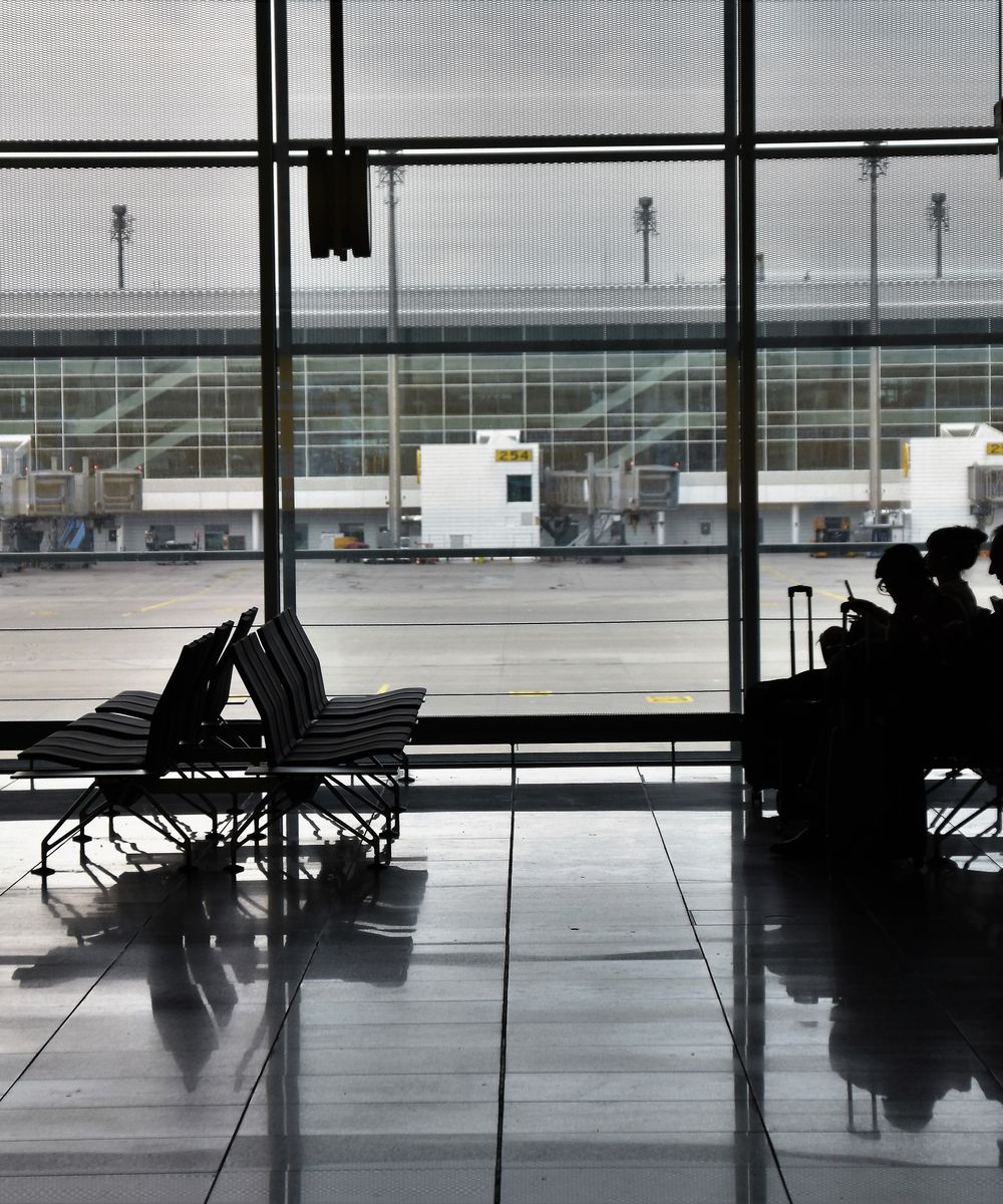 Travellers with luggage waiting beside a large airport window at dusk