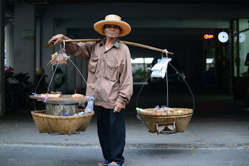 棕色夹克的男人，两个篮子吊在肩膀上的木杆