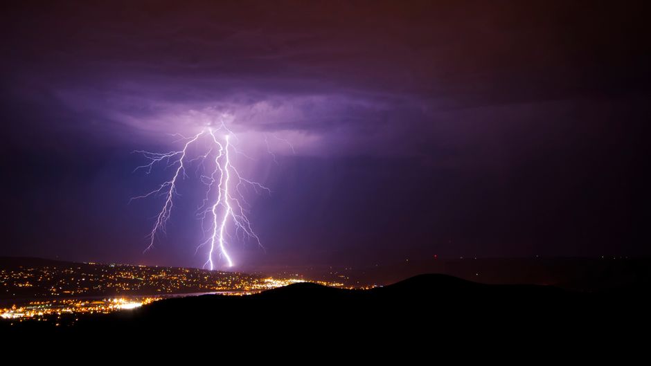 A powerful lightning bolt strikes during a night storm over Wenatchee, WA cityscape.