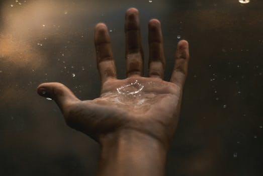 A close-up of an open hand catching raindrops against a dark background, showcasing water interaction.