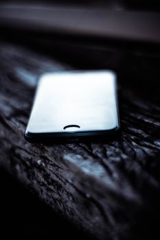 A blurred modern smartphone lying on a rustic wooden surface, showcasing selective focus.