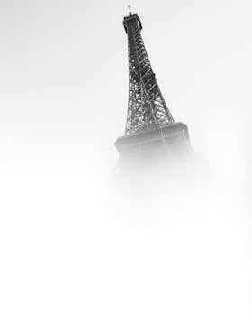 A foggy view of the Eiffel Tower emerging from the mist, capturing its iconic structure in a minimalist style.