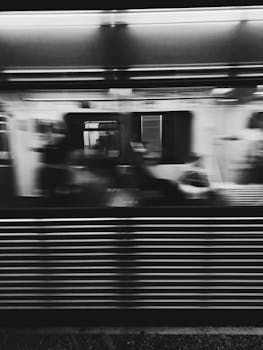 Blurred motion of a subway train speeding through a station in monochrome.