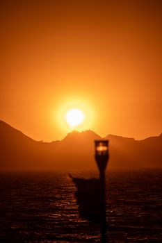 Captivating sunset in Cabo San Lucas with silhouetted hills and a lamp in the foreground.