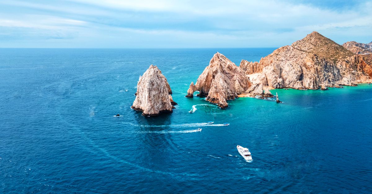Stunning aerial shot of Cabo San Lucas Arch with vibrant blue ocean and boats in view.