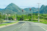 一条蜿蜒的高速公路，绿树成荫，背景是群山，沿途设有红绿灯