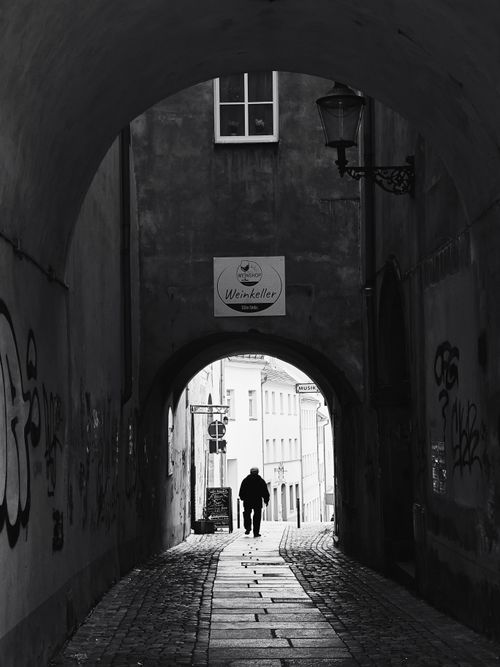 Free A solitary silhouette walks through a historic alley with arches, captured in black and white. Stock Photo