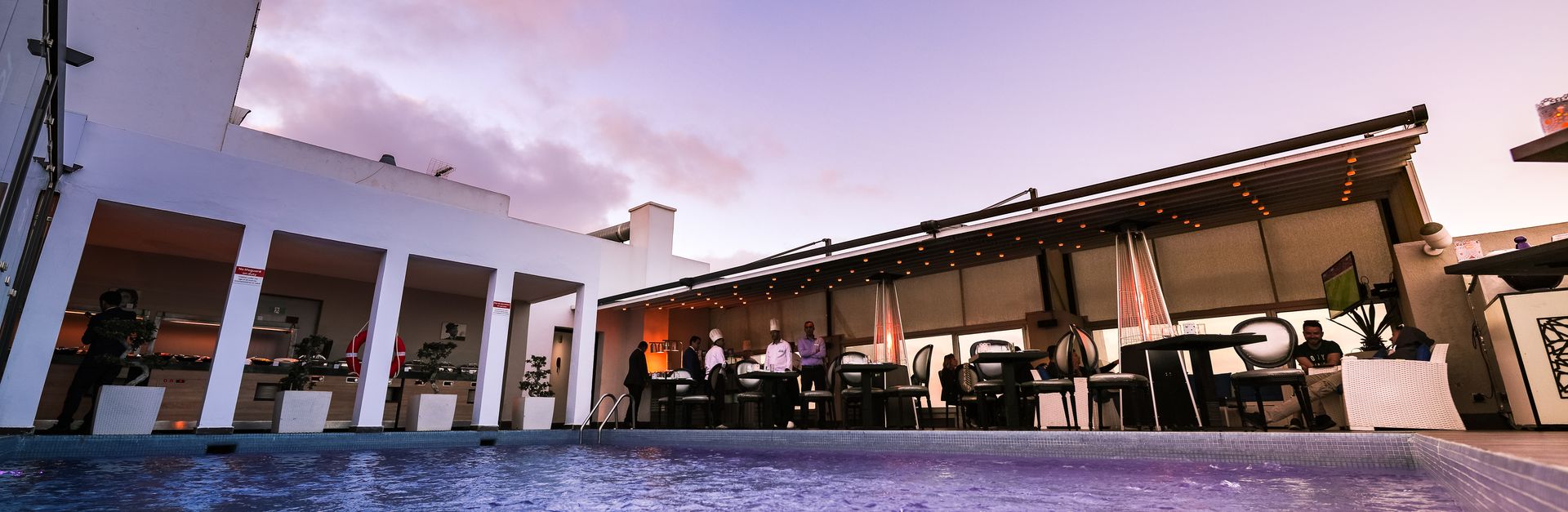 Vibrant rooftop pool and dining experience at sunset with elegant decor and ambient lighting.