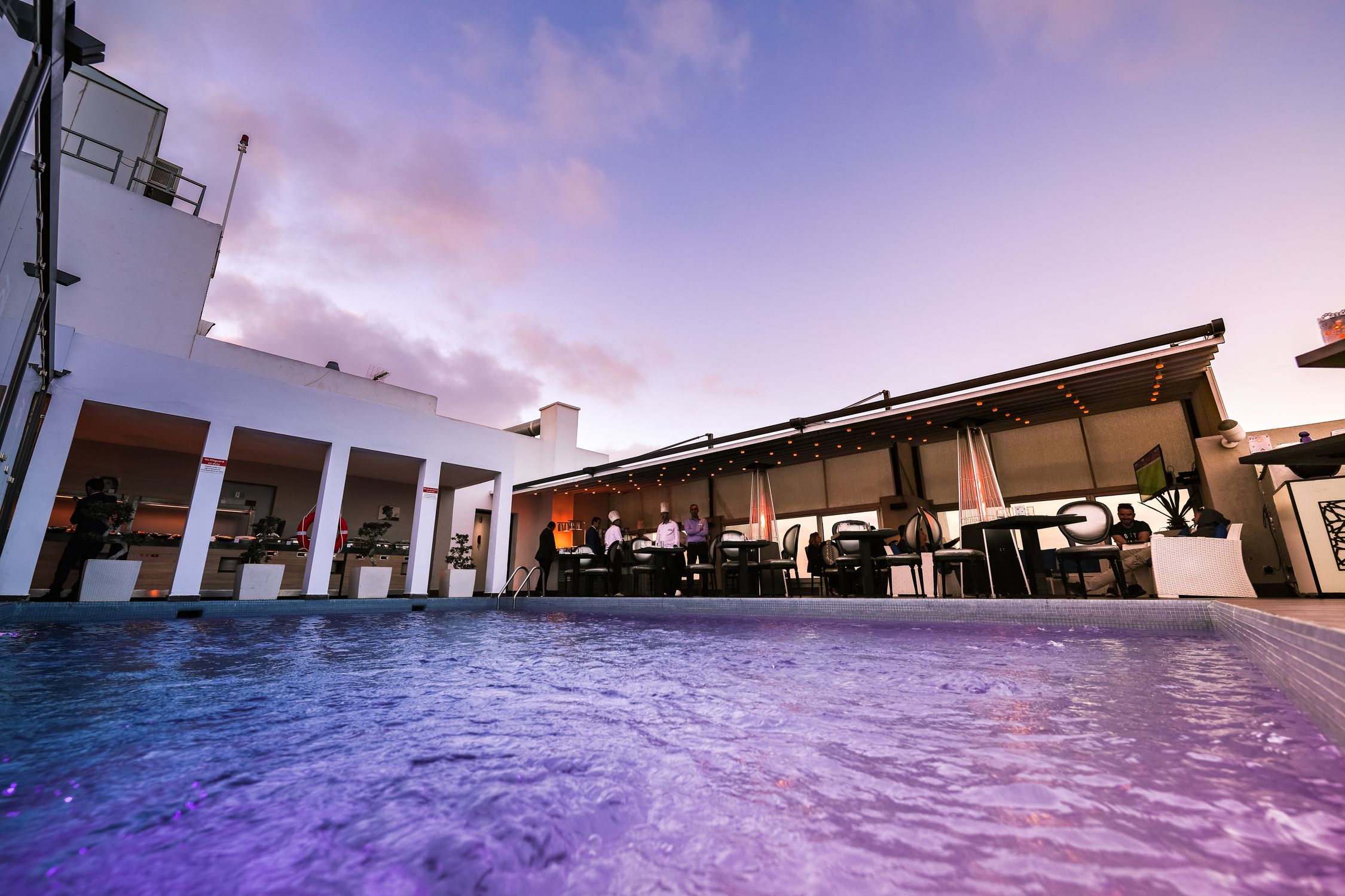 Vibrant rooftop pool and dining experience at sunset with elegant decor and ambient lighting.