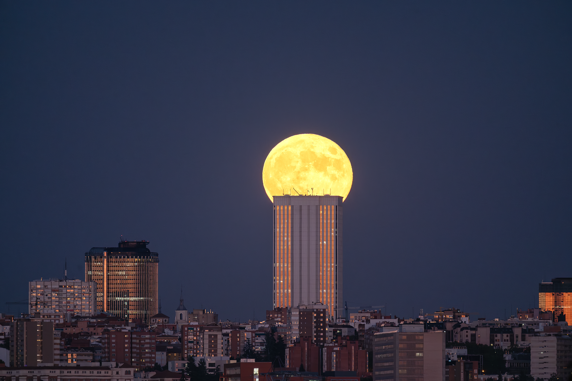 Luna llena anaranjada asomando sobre una línea de horizonte oscura al anochecer