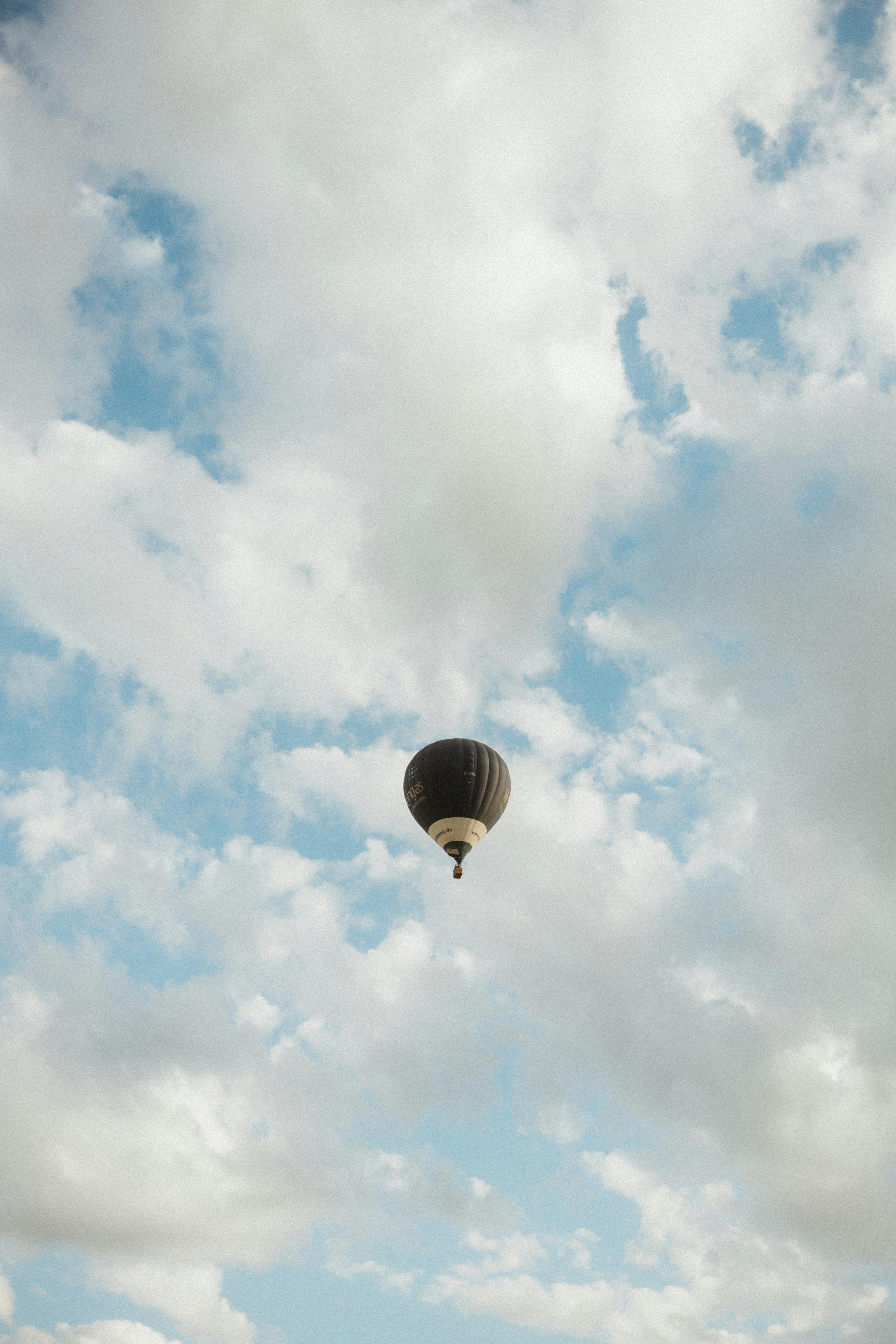 A lone hot air balloon floating serenely amidst fluffy clouds in a bright sky.