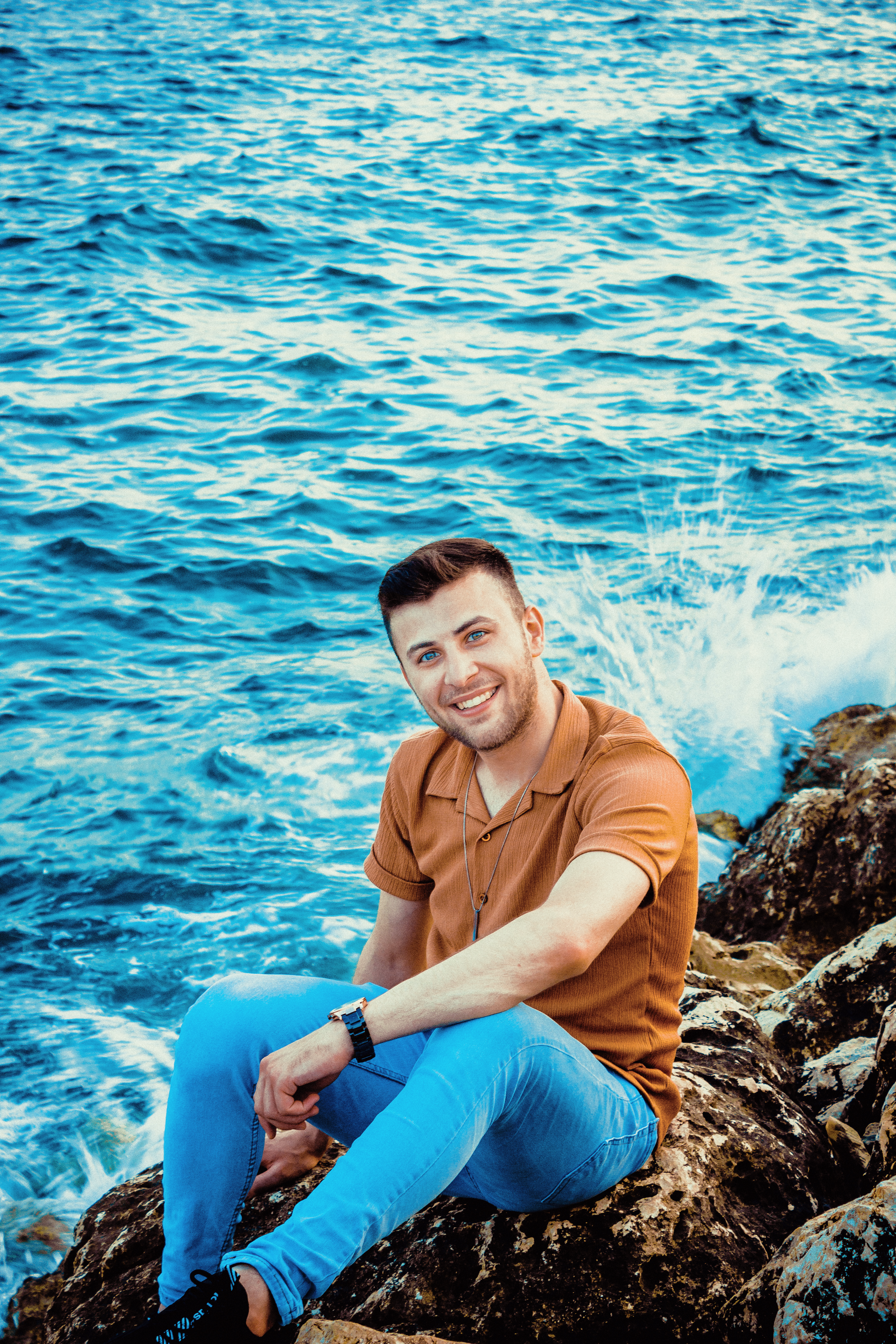 A Smiling Man Sitting on a Rocky Shore · Free Stock Photo