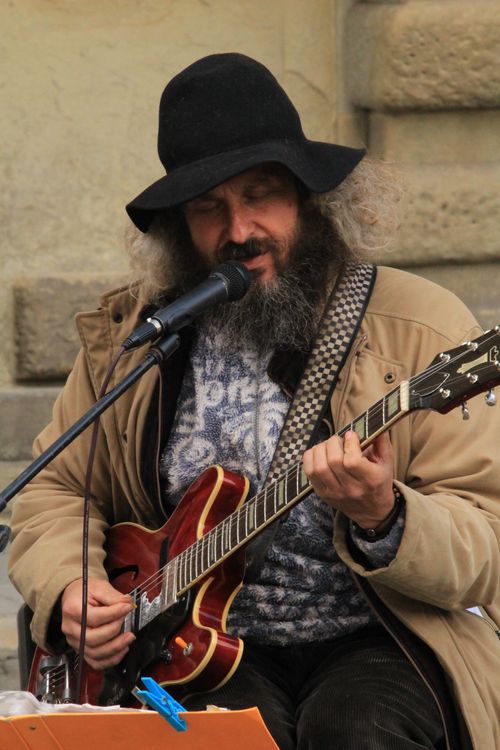 Free Street musician with a guitar and hat performing passionately in an urban setting. Stock Photo