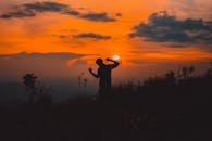 日落时分，田野里，一个人在充满活力的橙色天空下跳舞的剪影