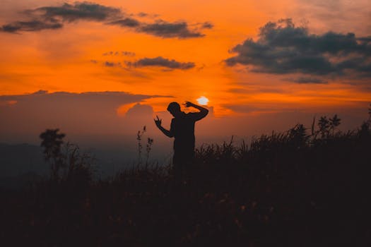 日落时分，田野里，一个人在充满活力的橙色天空下跳舞的剪影