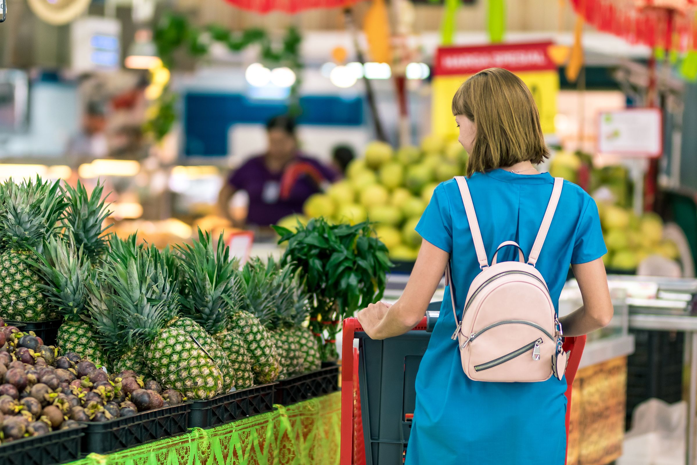 A shopper seen from behind, pushing a trolley through a busy market hall