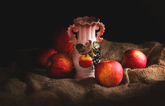 弱光下，粗麻布上描绘着红苹果的美丽静物画和华丽的陶瓷花瓶