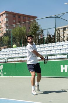 A man in sportswear playing tennis on an outdoor city court, swinging his racket mid-game.