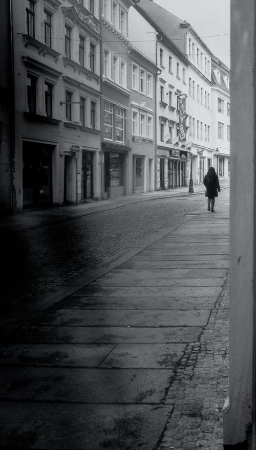 Free A lone figure walking down a quiet street in Zittau, Germany, captured in a black and white photograph. Stock Photo