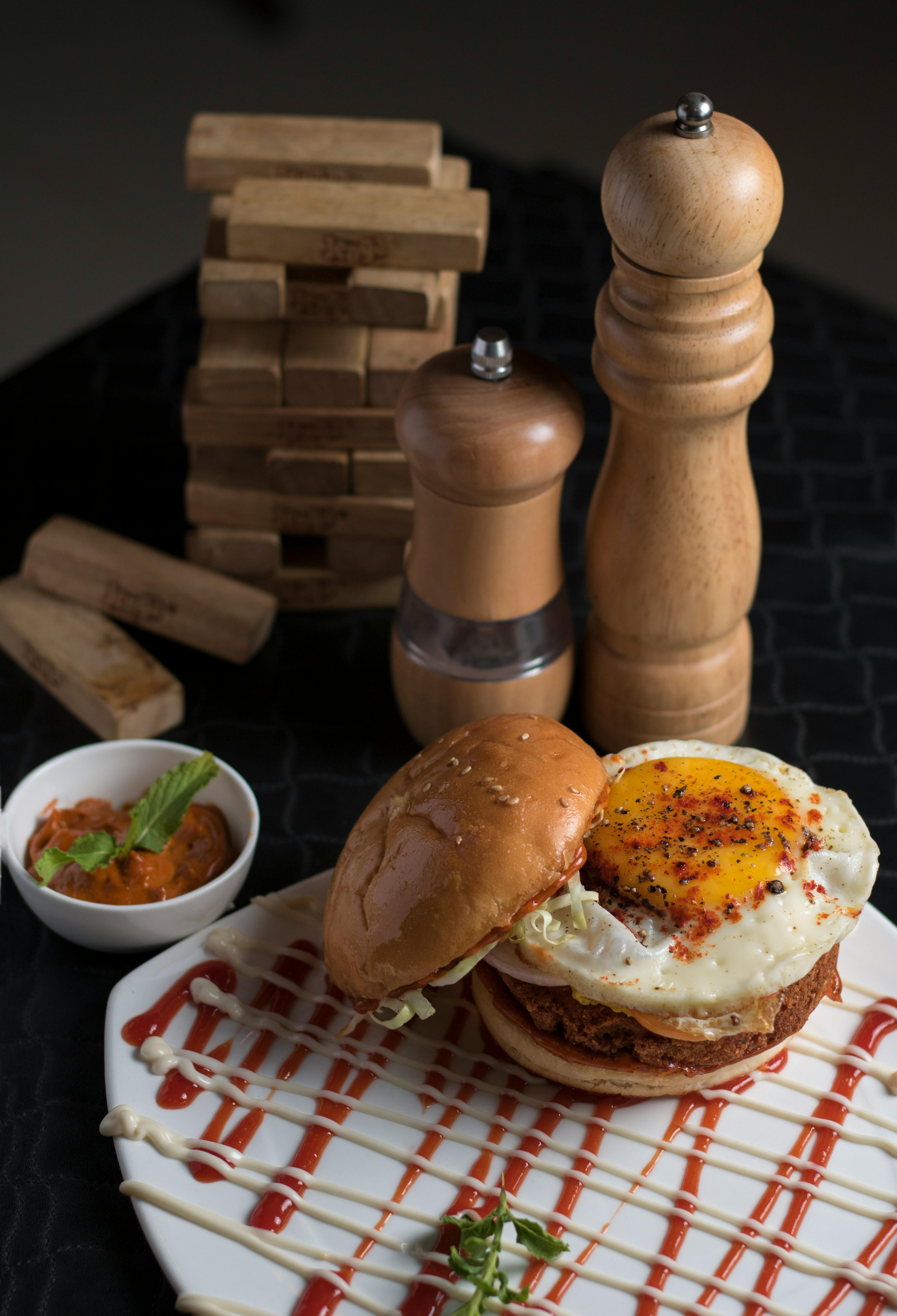 Delicious gourmet burger topped with a fried egg, accompanied by sauce and spices on a stylish plate.